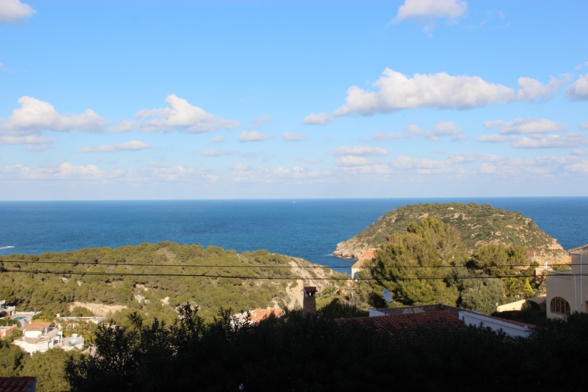 Panoramic view from the plot overlooking the Mediterranean Sea and Portichol Island, featuring lush green hillsides and traditional rooftops under a clear sky.