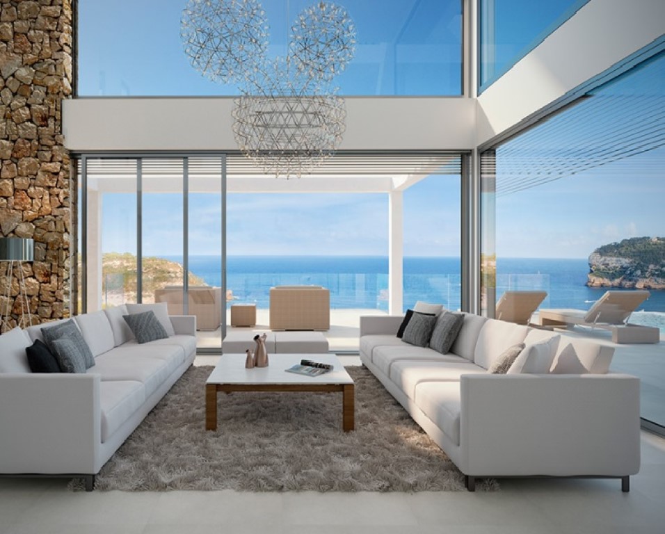 Double-height living room with floor-to-ceiling glass walls, a natural stone feature wall, and designer lighting overlooking the Mediterranean Sea.