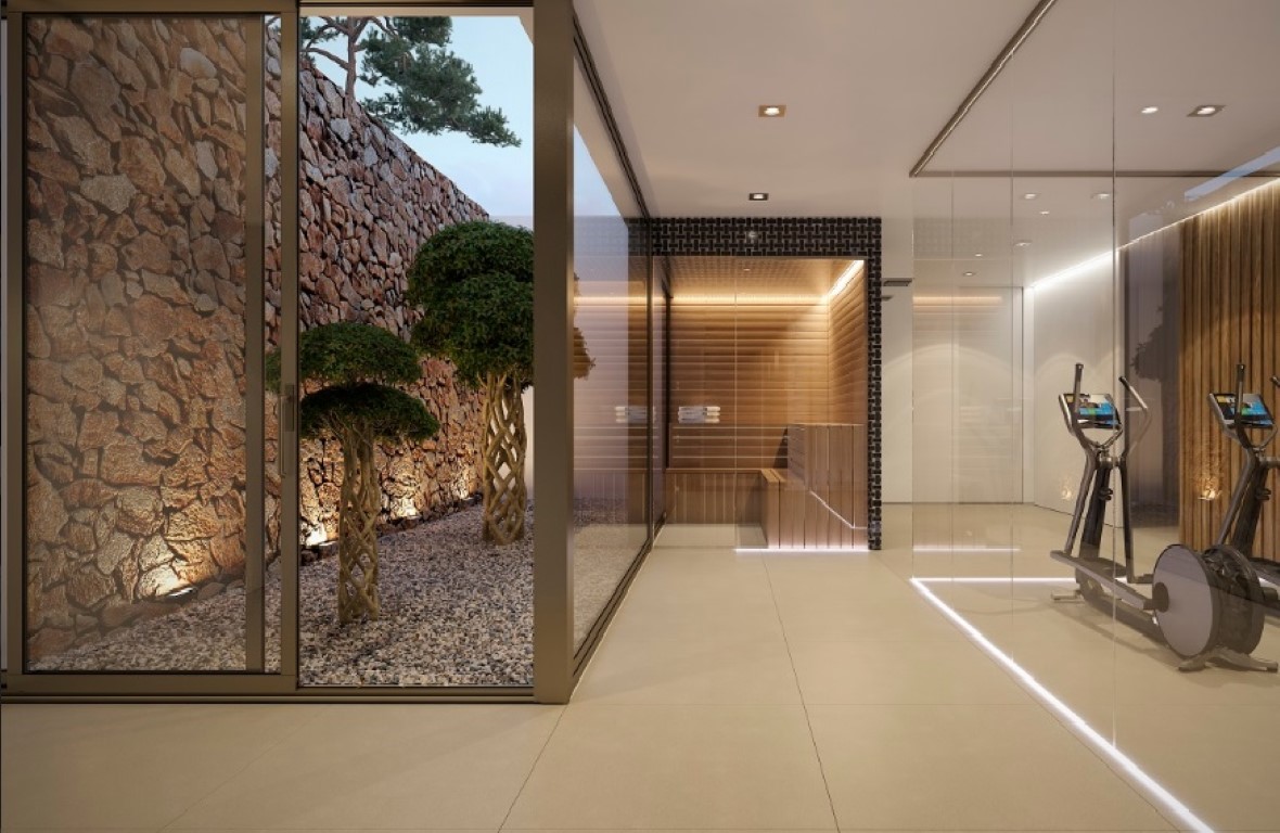 Wellness area featuring a glass-enclosed gym and wooden sauna, adjacent to an outdoor patio with a natural stone wall and sculpted trees.