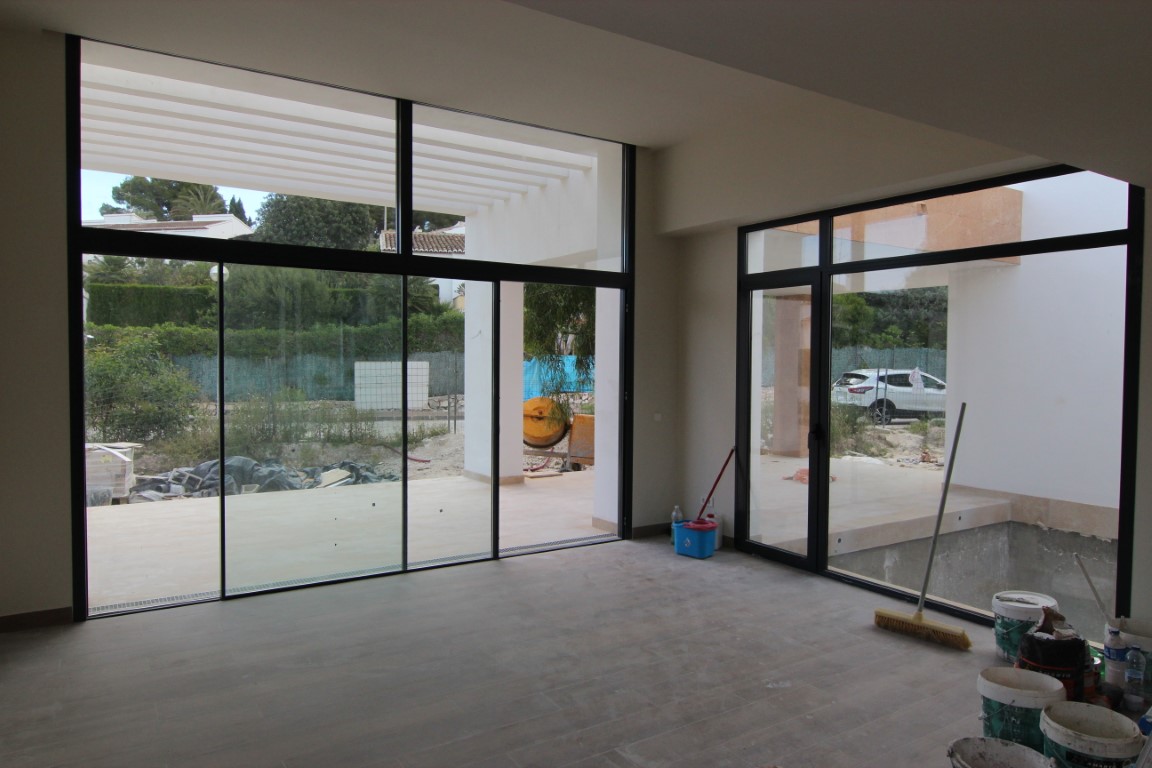 Living area under construction featuring floor-to-ceiling glass doors with black frames that open onto a terrace with a white pergola.