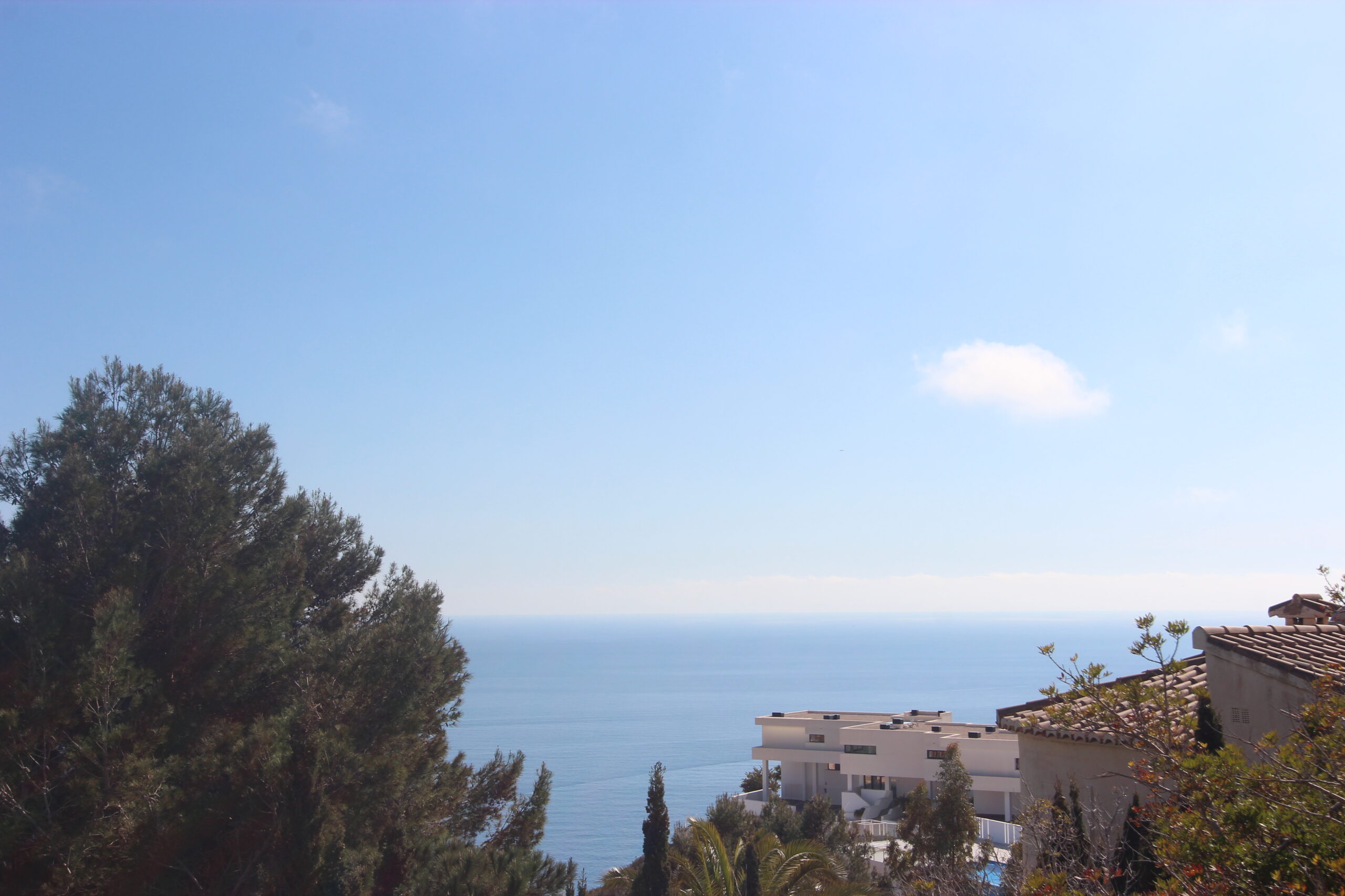 Panoramic Mediterranean Sea views from the property, framed by mature pine trees and modern white villas under a clear blue sky.