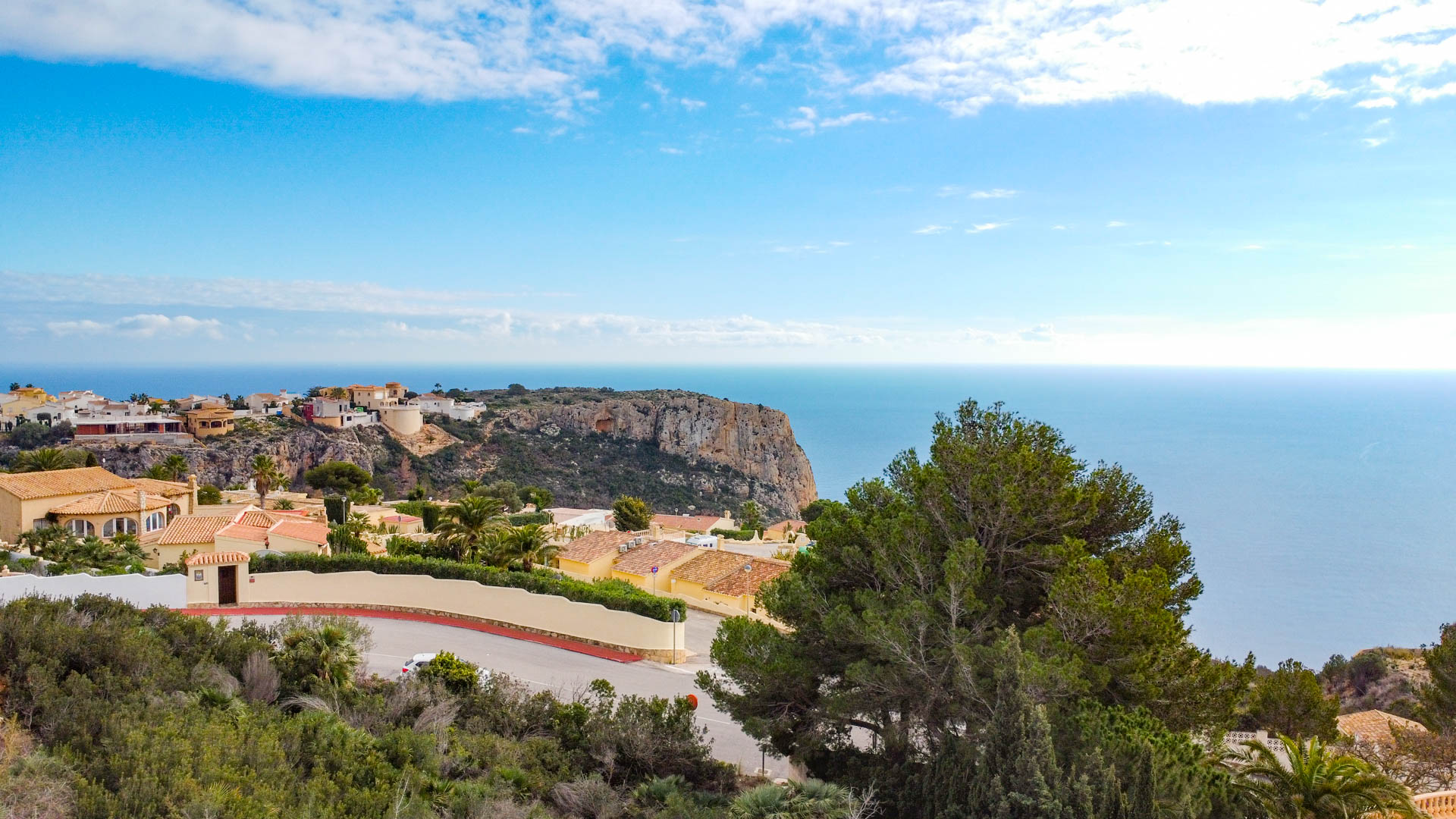 Panoramic view from Cumbre del Sol featuring the Mediterranean coastline, rugged cliffs, and residential villas nestled among green hillsides.