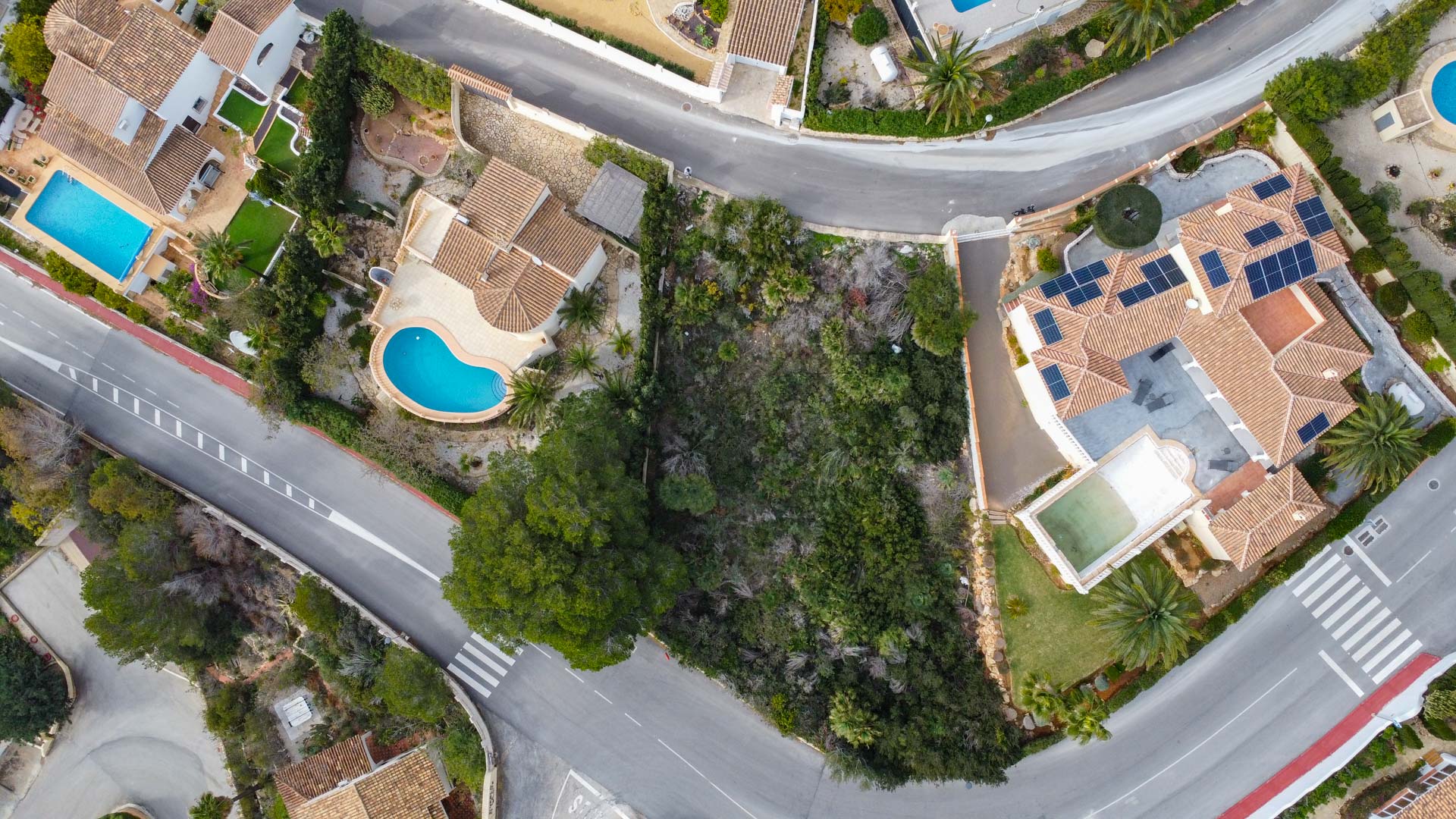 Zenith aerial view showcasing the residential layout, traditional Mediterranean tiled roofs, private swimming pools, and integrated solar panel systems.