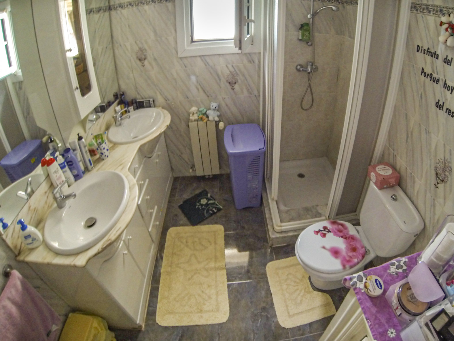 Bathroom featuring dual sinks, a shower with a screen, and a toilet with a decorated lid.