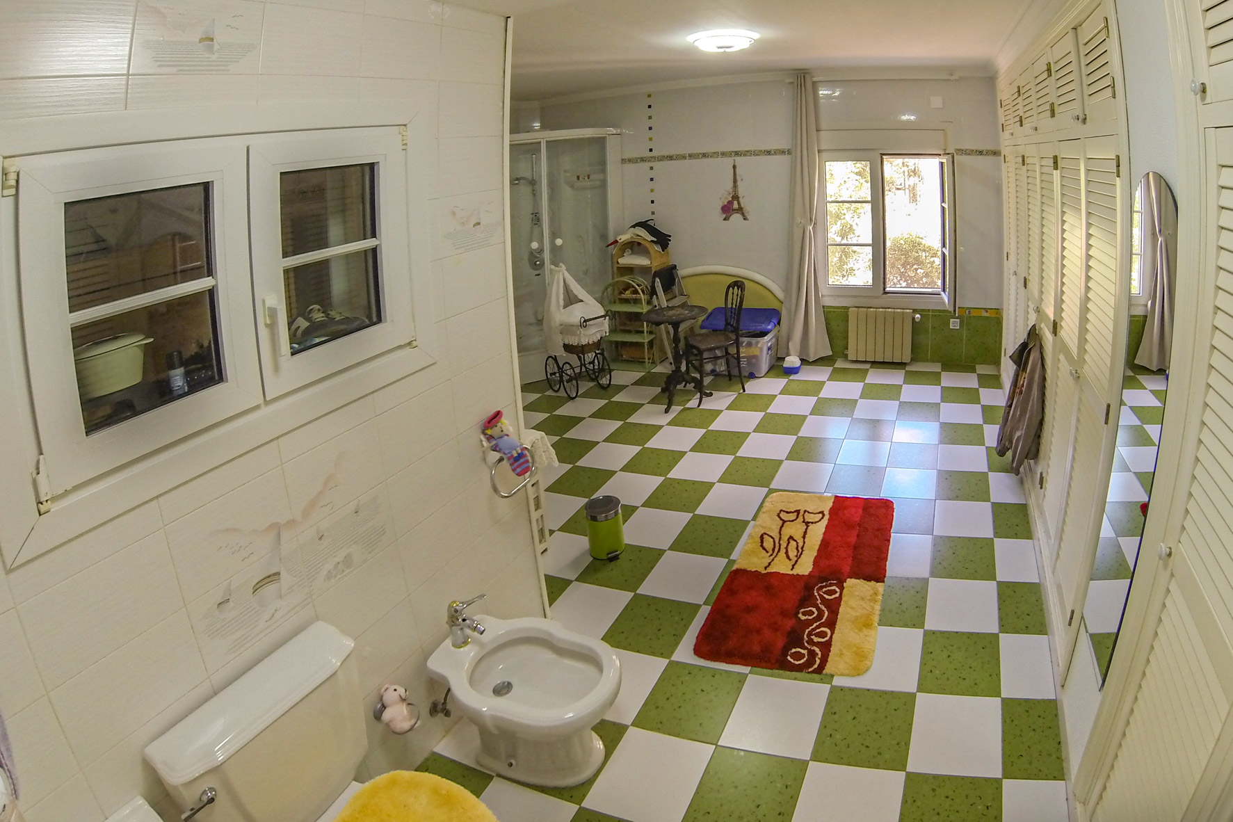 Bathroom featuring green and white tiled floors, white toilet and bidet, and a window providing natural light.