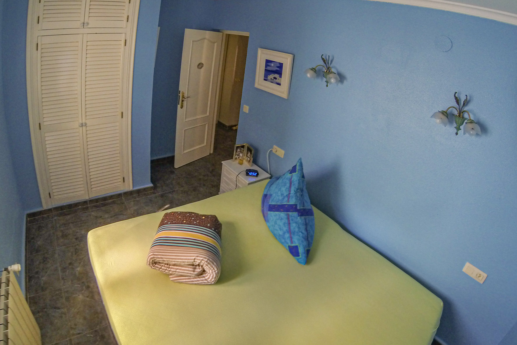 Bedroom with blue walls, a built-in white wooden wardrobe, and folded bedding.