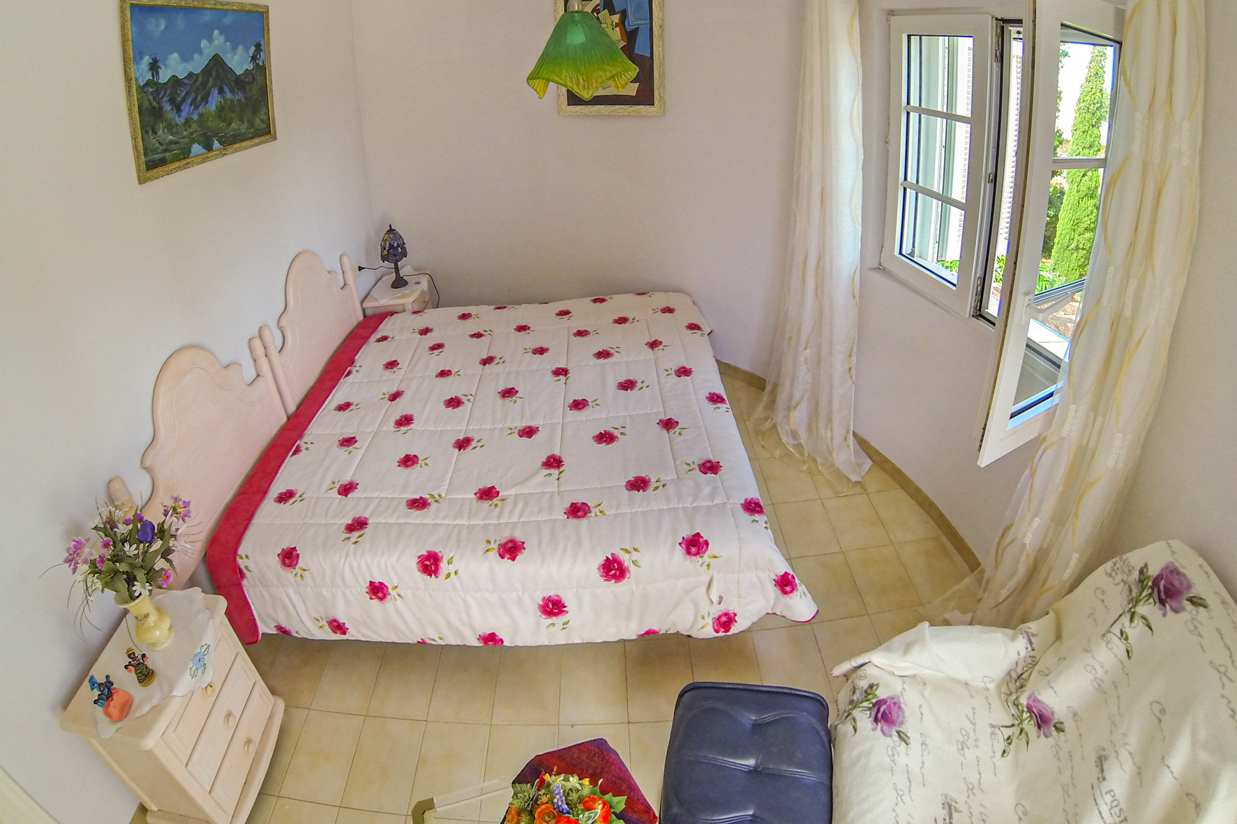 Bright bedroom featuring a double bed, floral bedding, and a window with sheer curtains.