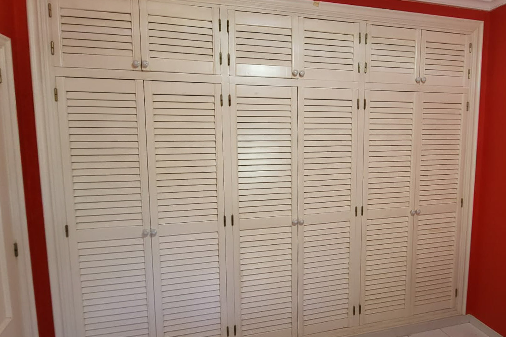 Built-in wardrobe with shutter doors in bedroom with red wall.