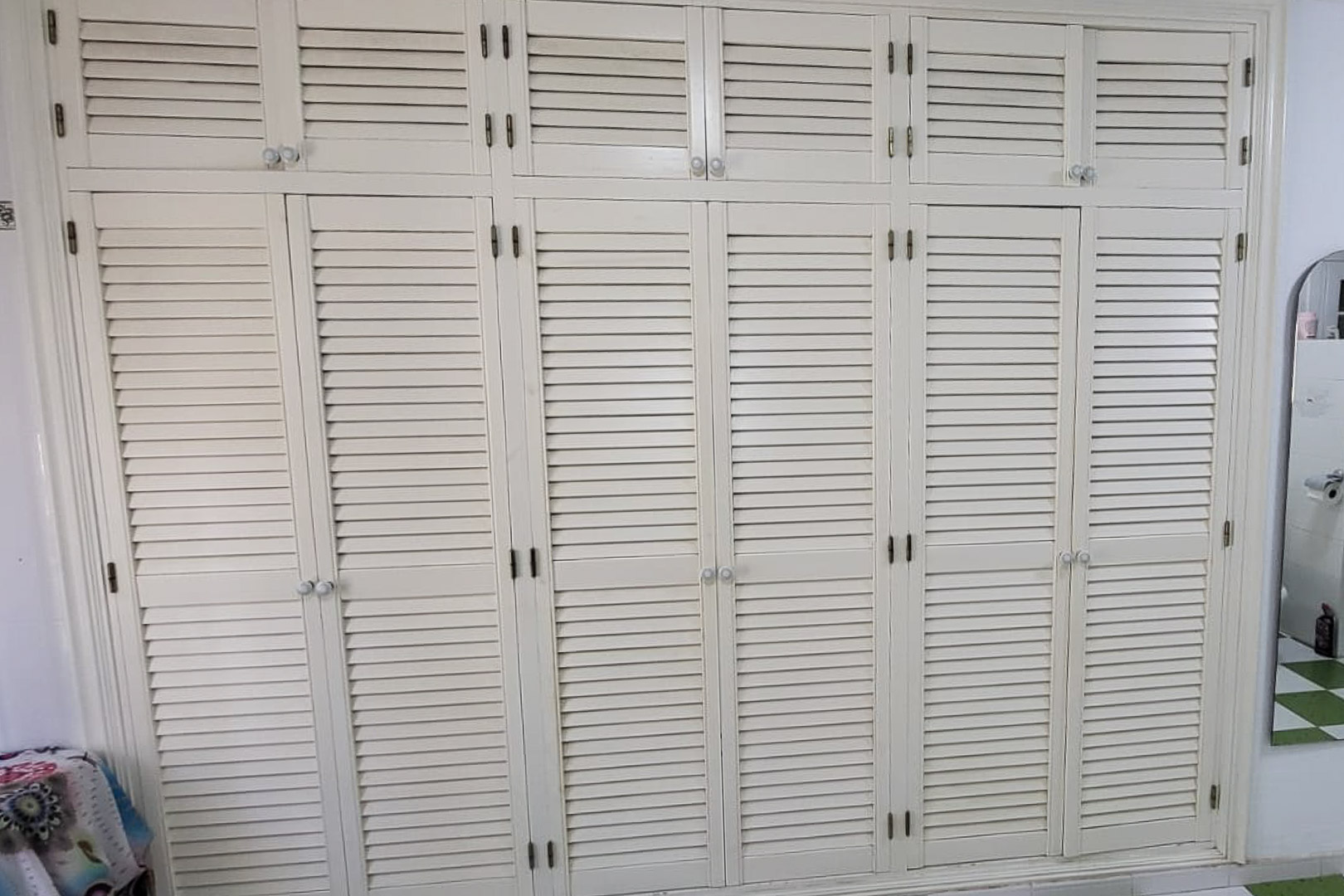 Built-in wooden wardrobe with shutter doors and round knobs, spanning the entire wall.
