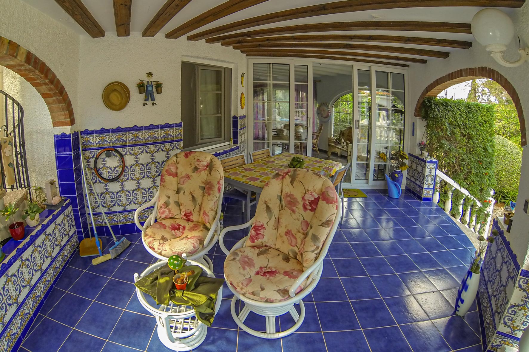 Covered porch with blue tile, brick arches, and floral chairs.
