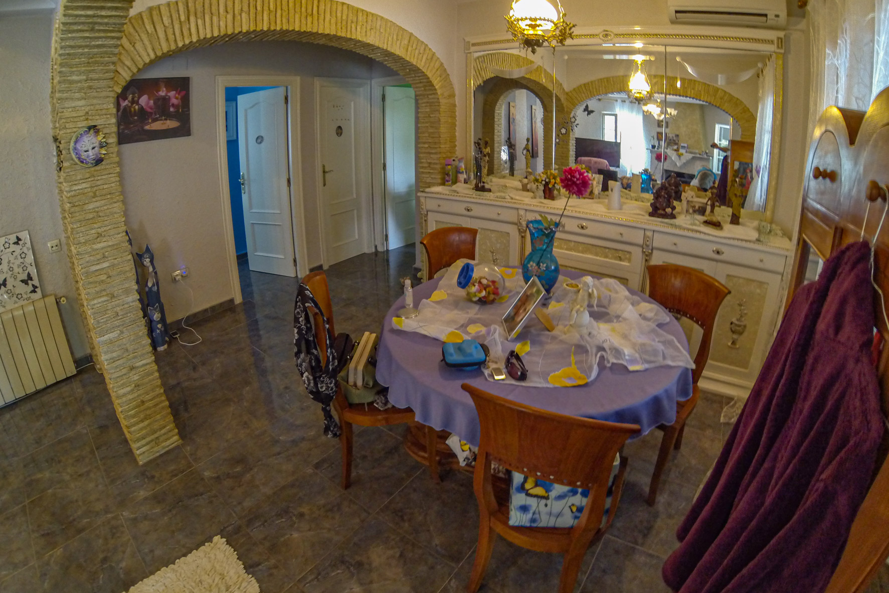 Dining area featuring stone arches, a round table with a lilac tablecloth, and an ornate white sideboard with a mirror.
