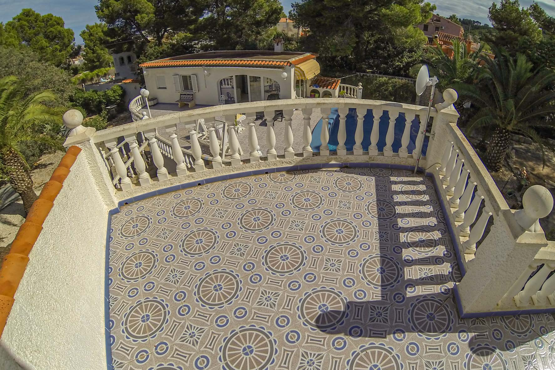 Terrace with patterned tiles and a white railing overlooking the property and greenery.