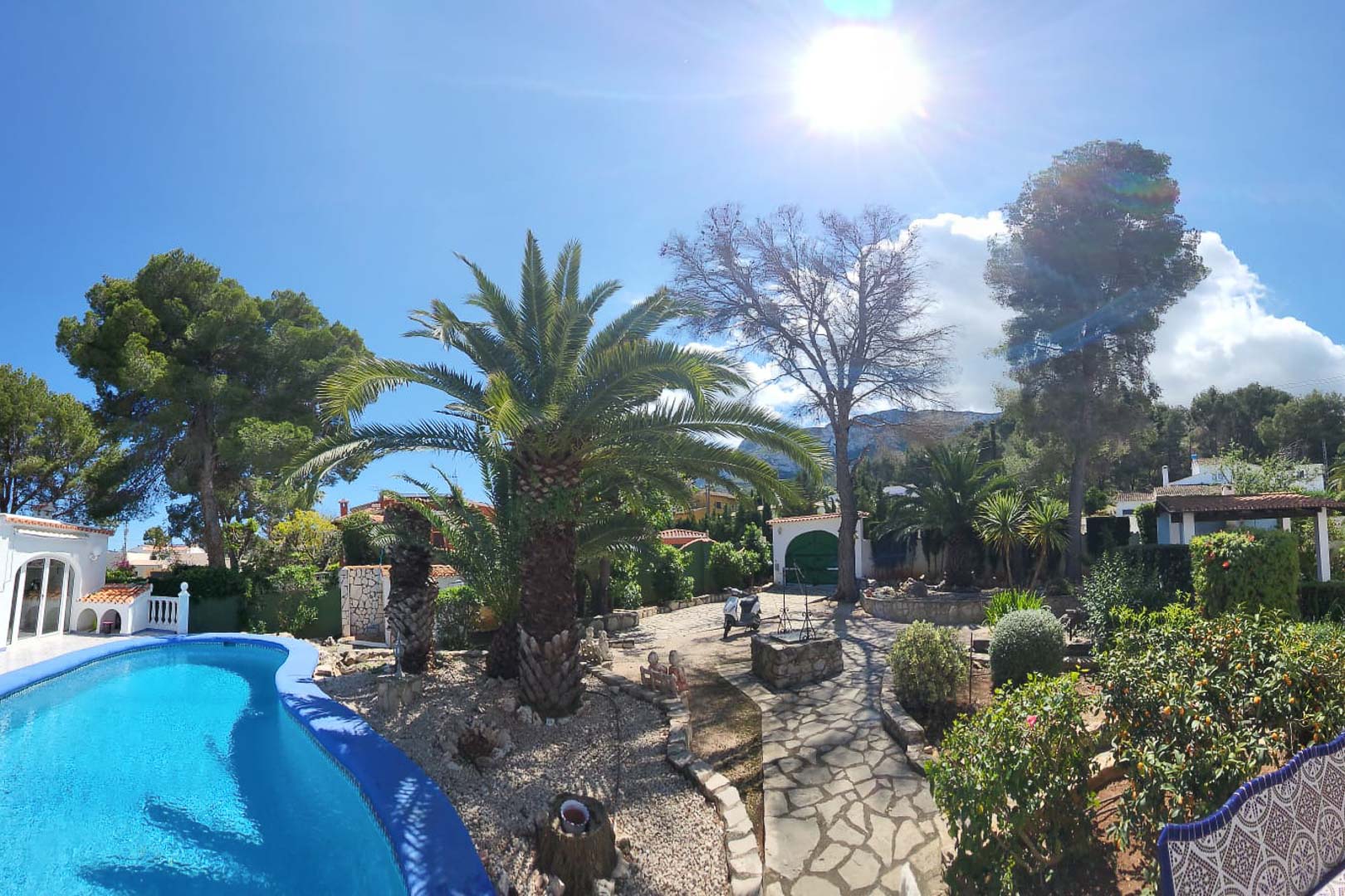 View of the turquoise blue pool and gardens with palm trees and stone path in Denia.