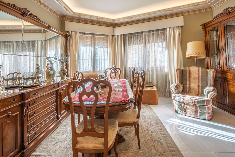Classic dining room featuring carved wooden furniture, a glass-top table, mirrored sideboard, and decorative ceiling moldings with recessed lighting.