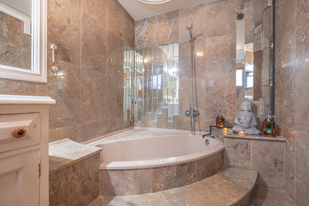Elegant bathroom featuring a built-in corner bathtub, polished marble wall tiles, and a unique vertical mirror arrangement.