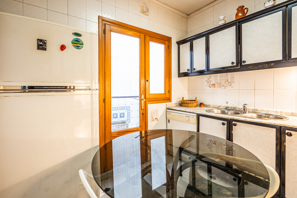 Functional kitchen featuring dark-trimmed cabinetry, marble countertops, and a glass-paneled wooden door leading to a private patio. Includes a glass-top dining table.