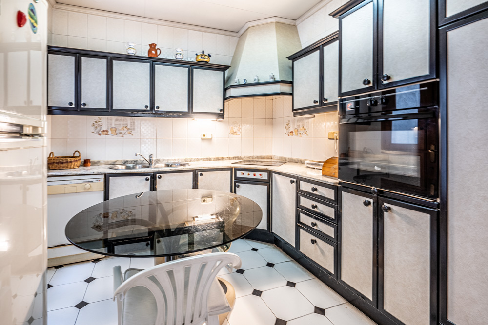 Functional kitchen featuring white cabinetry with dark framing, integrated appliances, a marble countertop, and a glass dining table set on patterned tile flooring.