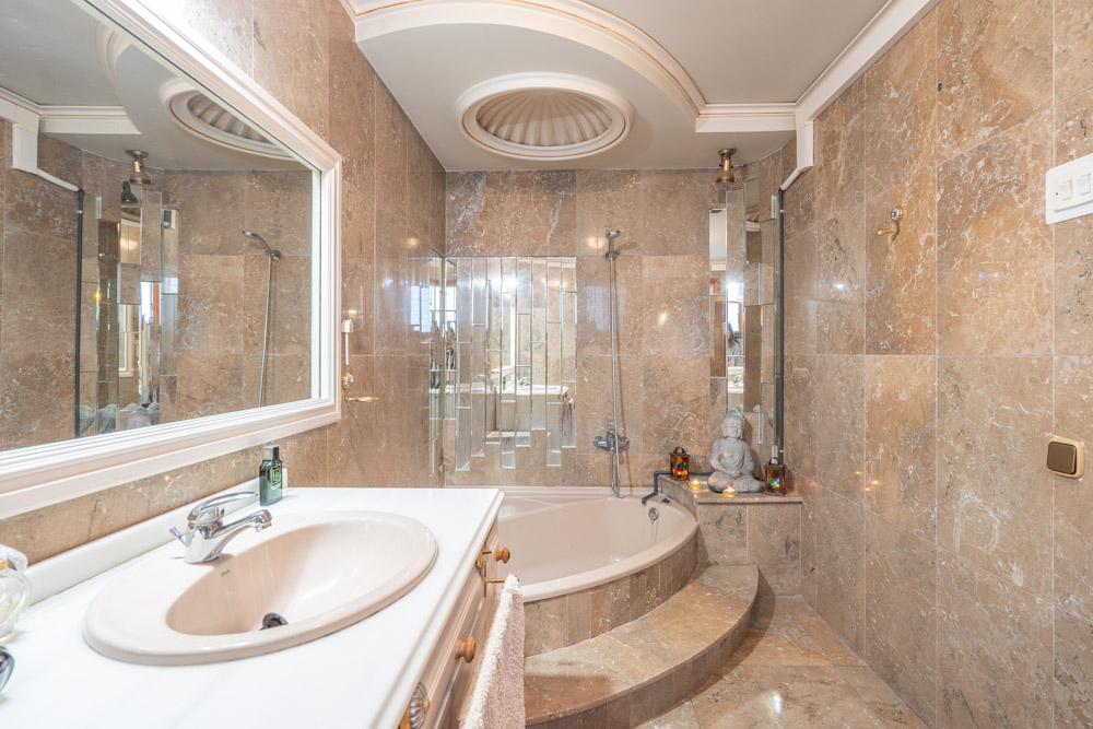 Marble-clad bathroom featuring a built-in oval bathtub with a step, a white vanity unit, and a distinctive recessed circular ceiling design.