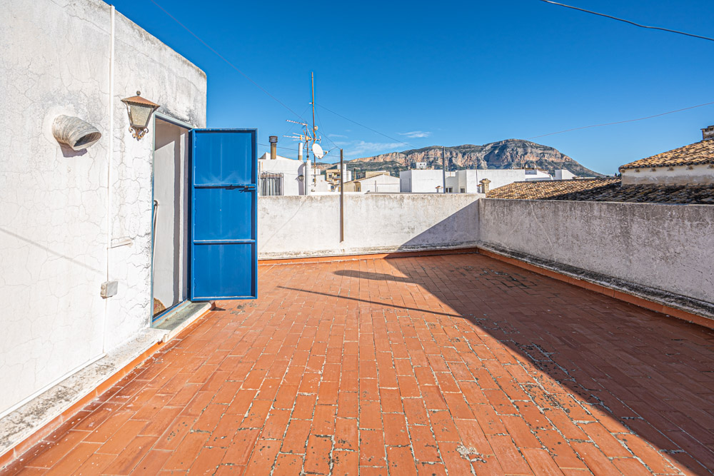 Rooftop terrace featuring traditional terracotta tiling, a blue metal access door, and panoramic views of the Montgó mountain range.