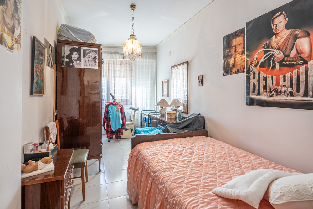 Single bedroom featuring a dark wood wardrobe, vanity desk, and tiled flooring. Natural light filters through the window, highlighting the traditional layout.