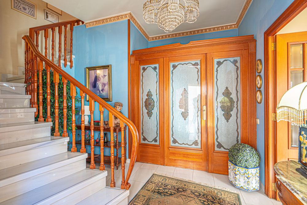 Spacious foyer featuring a marble staircase with wooden railings. Decorative elements include etched glass doors, ornate crown molding, and a central crystal chandelier.