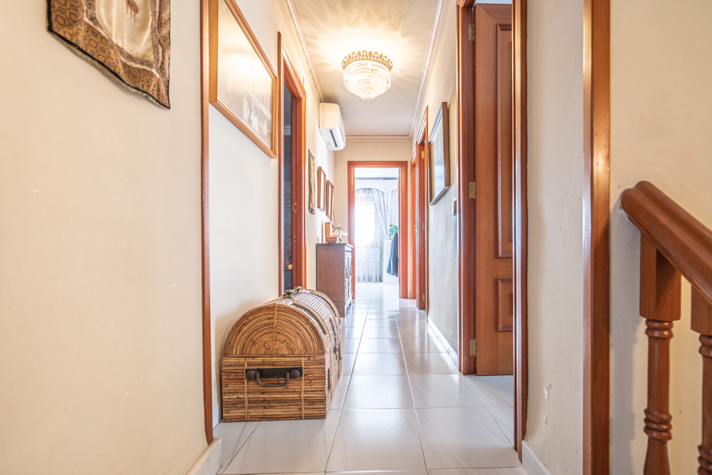 Upper floor hallway featuring light tiled flooring, solid wood doors, and a classic crystal chandelier. Includes split-system air conditioning and decorative wicker chest.