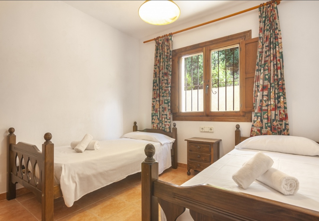 Bedroom featuring twin wooden beds with traditional carvings, terracotta tile flooring, and a window with rustic wooden shutters.