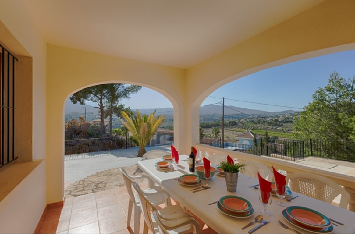 Covered terrace featuring traditional arches, an outdoor dining area, and panoramic views of the green valley and distant mountains.
