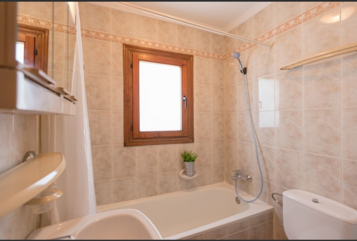 Functional bathroom featuring a built-in bathtub, beige tiled walls with a decorative border, and a wooden-framed window providing natural light.