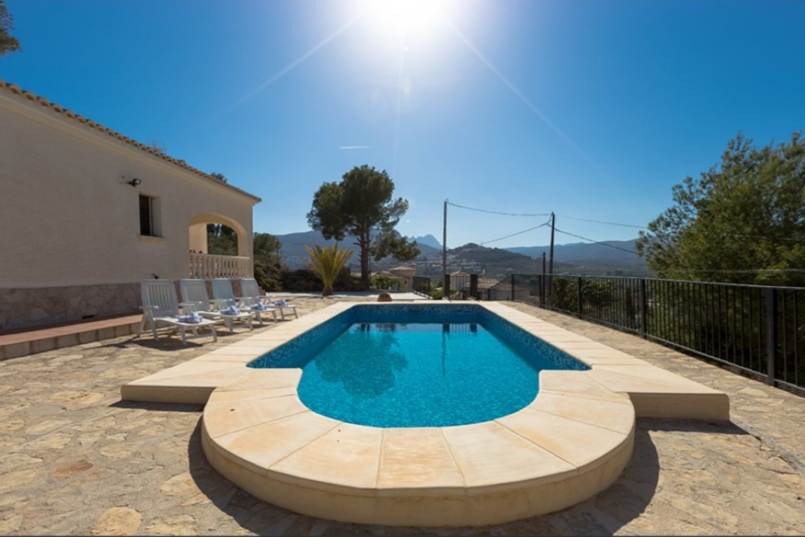 Outdoor swimming pool with a stone-paved terrace and panoramic mountain views. Features white sun loungers and a black metal safety railing.