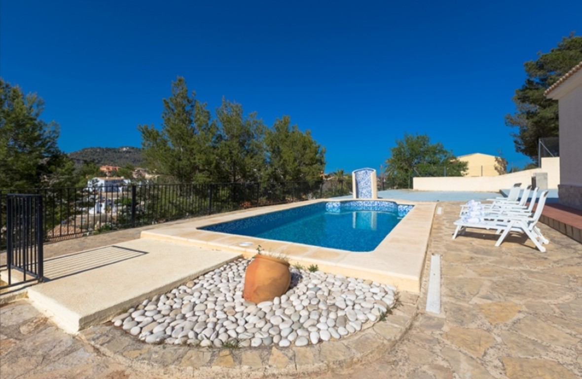 Stone-paved terrace featuring a rectangular swimming pool with white loungers, offering clear views of the surrounding hills and greenery.