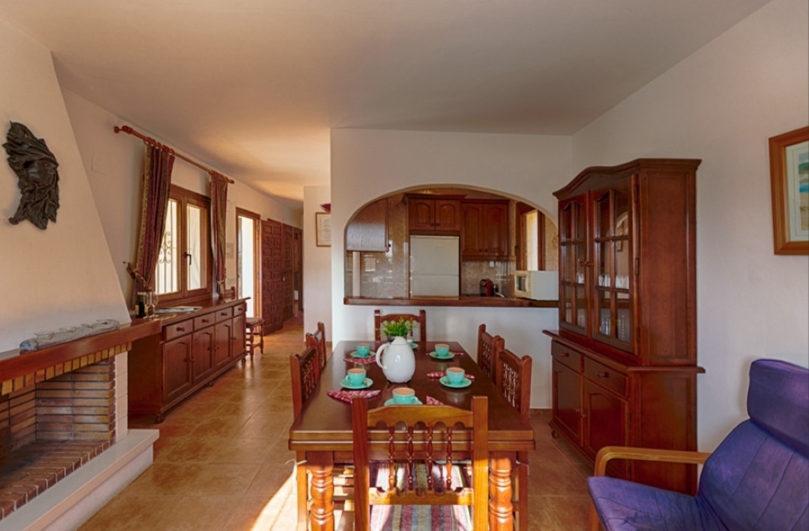 Traditional dining area featuring a brick fireplace, solid wood furniture, and tiled flooring. An arched opening provides a view into the adjacent kitchen.