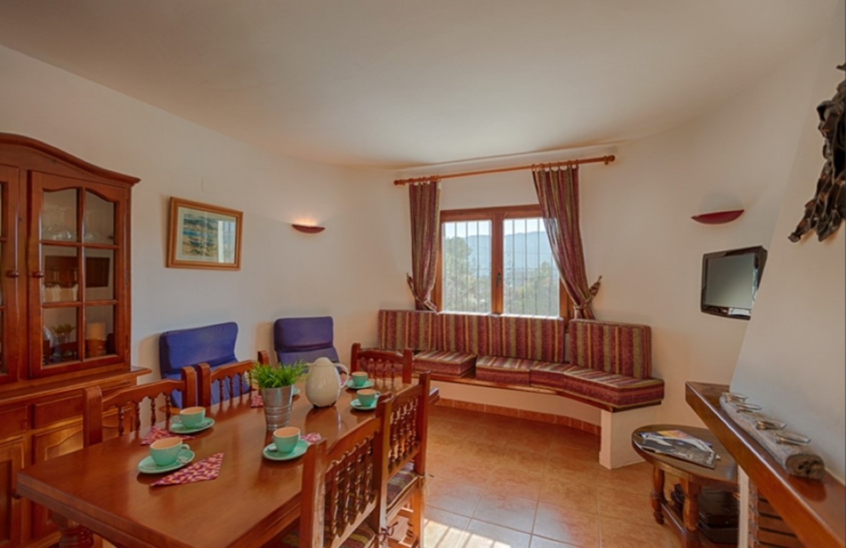 Traditional dining area featuring a wooden table set, a classic display cabinet, and a built-in cushioned bench under a window with countryside views.