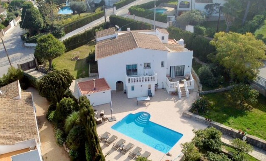 Aerial view of the villa featuring a private swimming pool, spacious sun terrace with loungers, and landscaped gardens surrounding the traditional white facade.