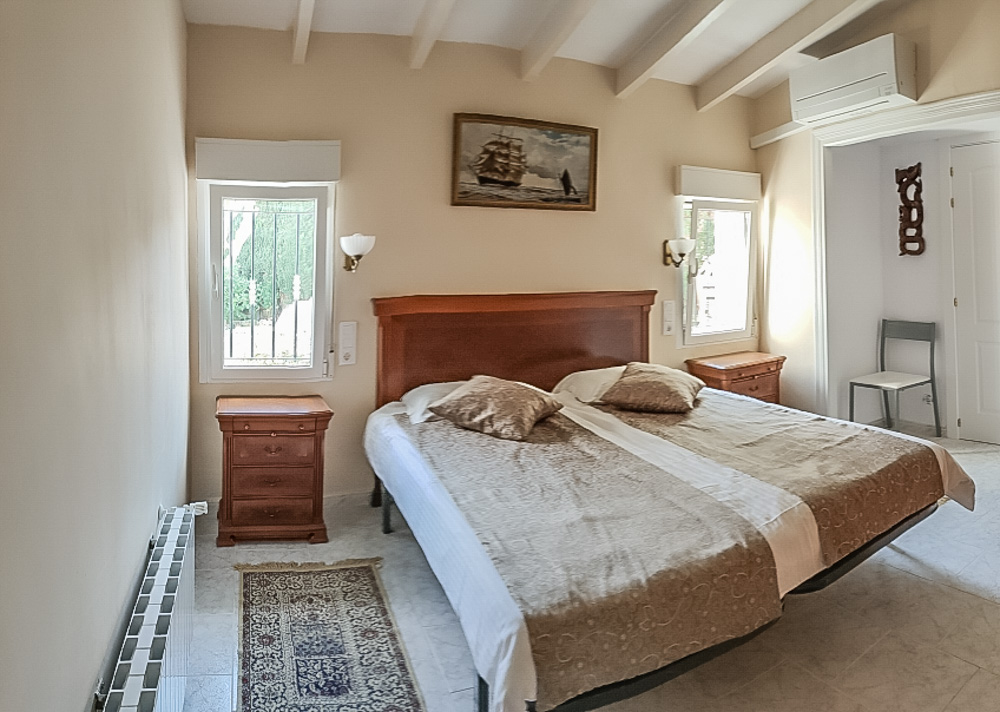 Bedroom featuring white beamed ceilings, a wooden headboard with matching nightstands, split-system air conditioning, and radiator heating.