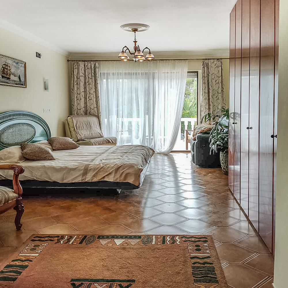 Bright bedroom featuring floor-to-ceiling wooden wardrobes, patterned tile flooring, and large sliding doors opening onto a private terrace.