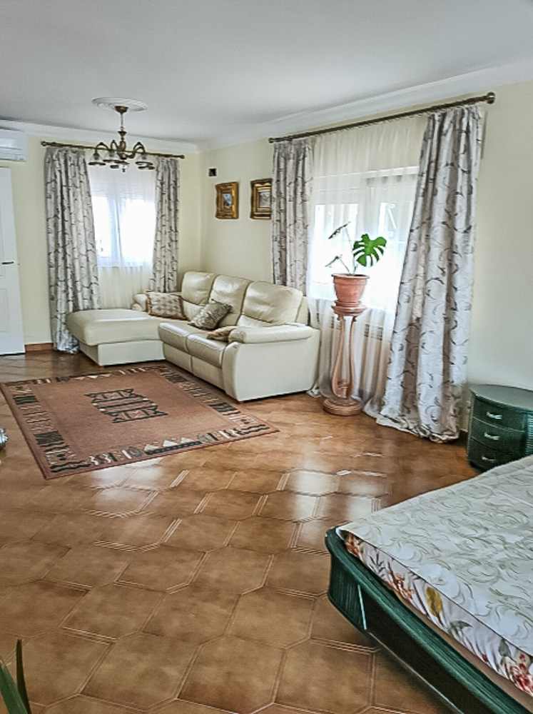 Bright living area featuring decorative ceramic tile flooring, a cream leather sofa, and large windows with patterned drapery providing natural light.