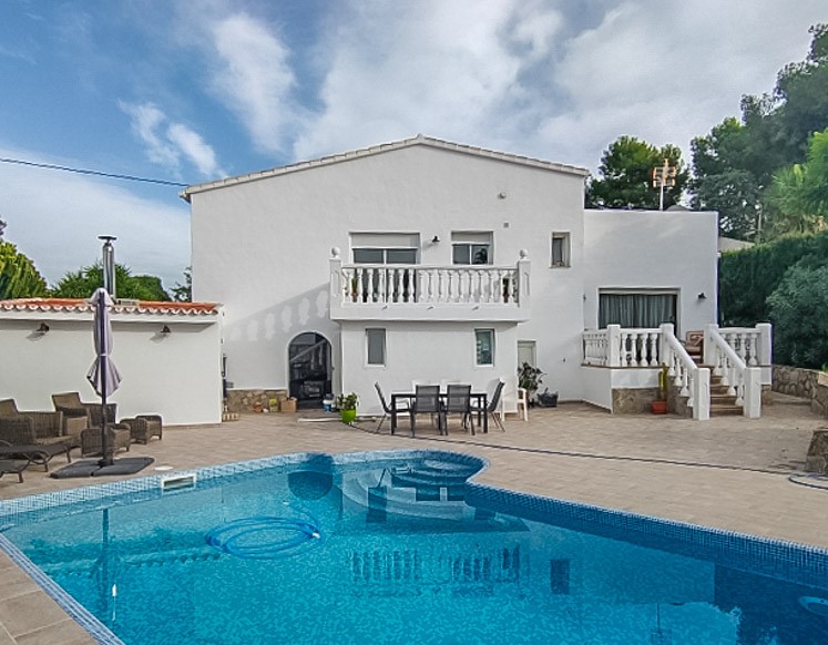 Exterior view featuring a blue mosaic pool, spacious tiled terrace, and the white multi-level villa facade with traditional balustrades and outdoor seating.