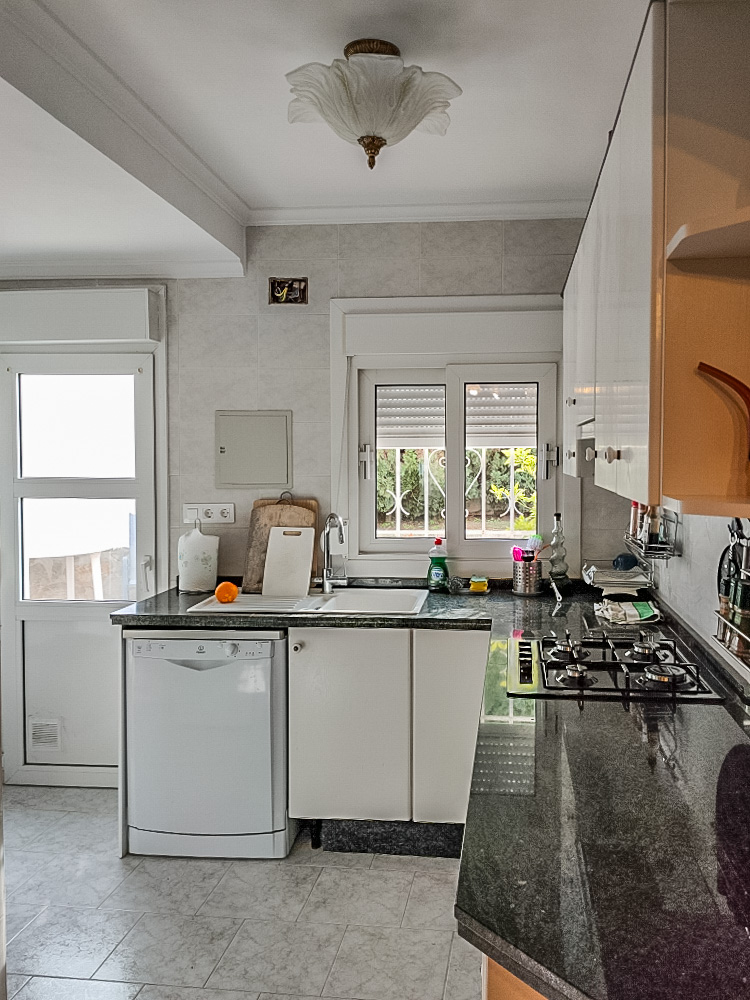 Practical kitchen featuring dark granite countertops, a gas stove, and white cabinetry. It includes a dishwasher and direct access to the exterior via a glazed door.