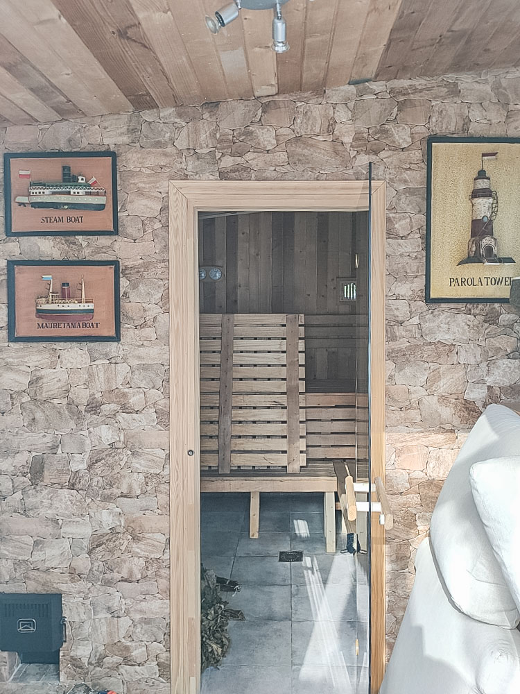 Private sauna featuring natural stone wall cladding and a glass door. The interior is fully finished in wood with multi-level seating and temperature gauges.