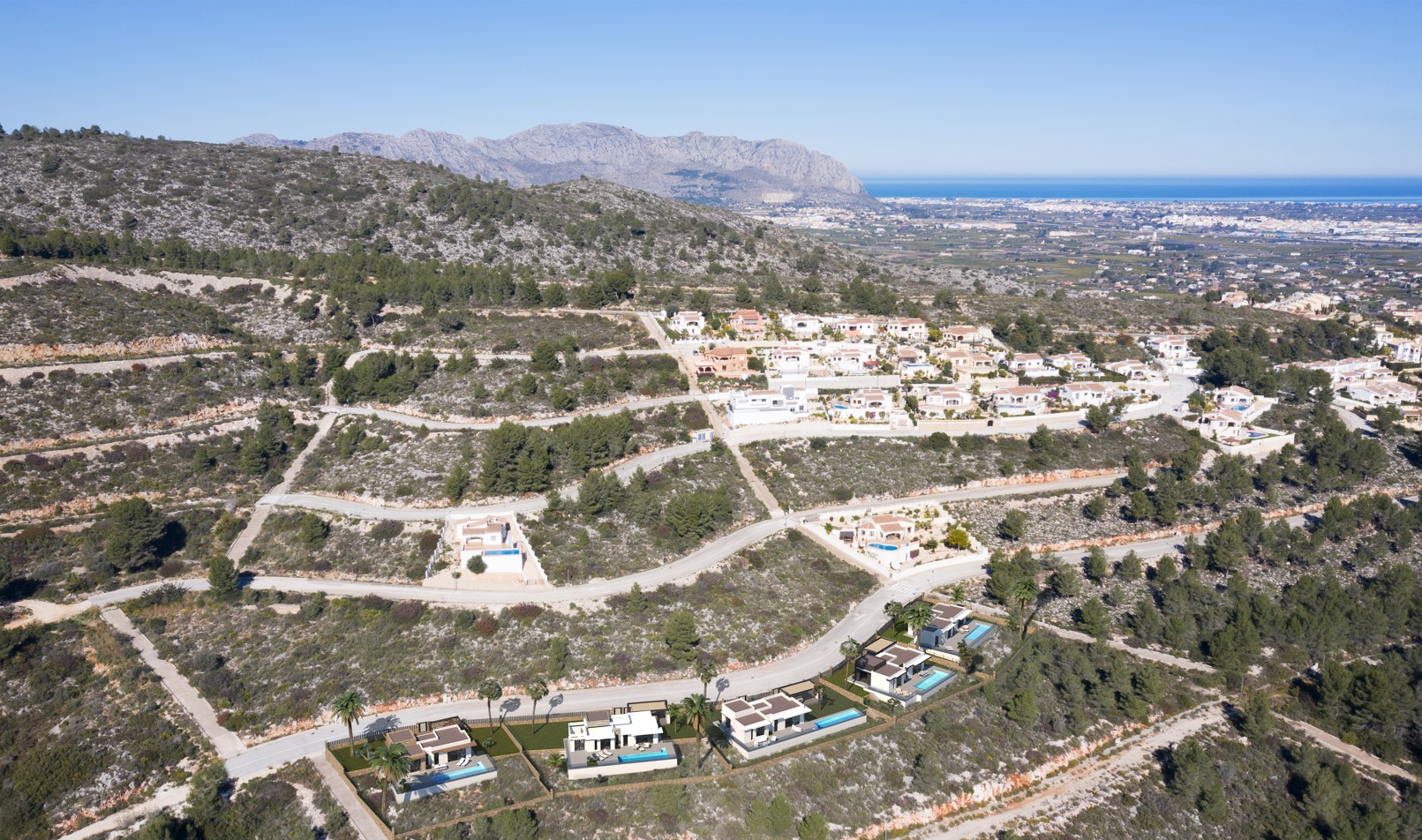 Aerial view of the Pedreguer hillside development, featuring modern villas with private pools and panoramic vistas of the Mediterranean coastline and mountains.