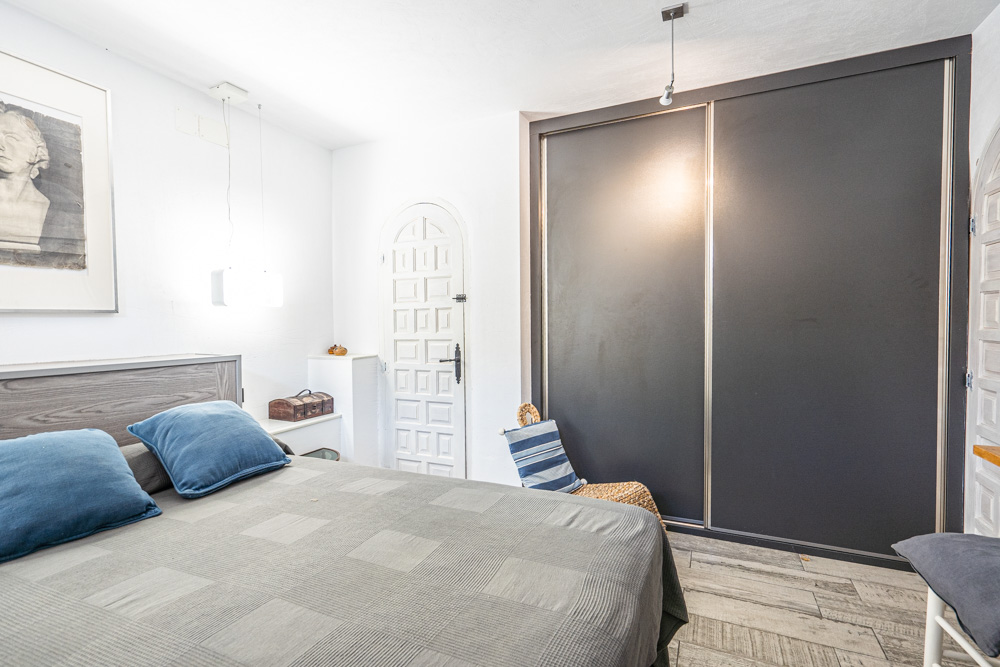 Bedroom featuring a large built-in wardrobe with dark sliding doors, wood-look tile flooring, and a traditional white arched interior door.