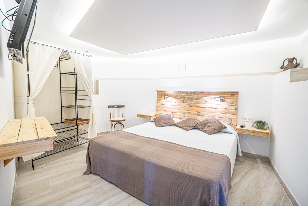 Bedroom featuring a rustic wood pallet headboard, floating nightstands, indirect ceiling lighting, and a minimalist open wardrobe with white curtains.