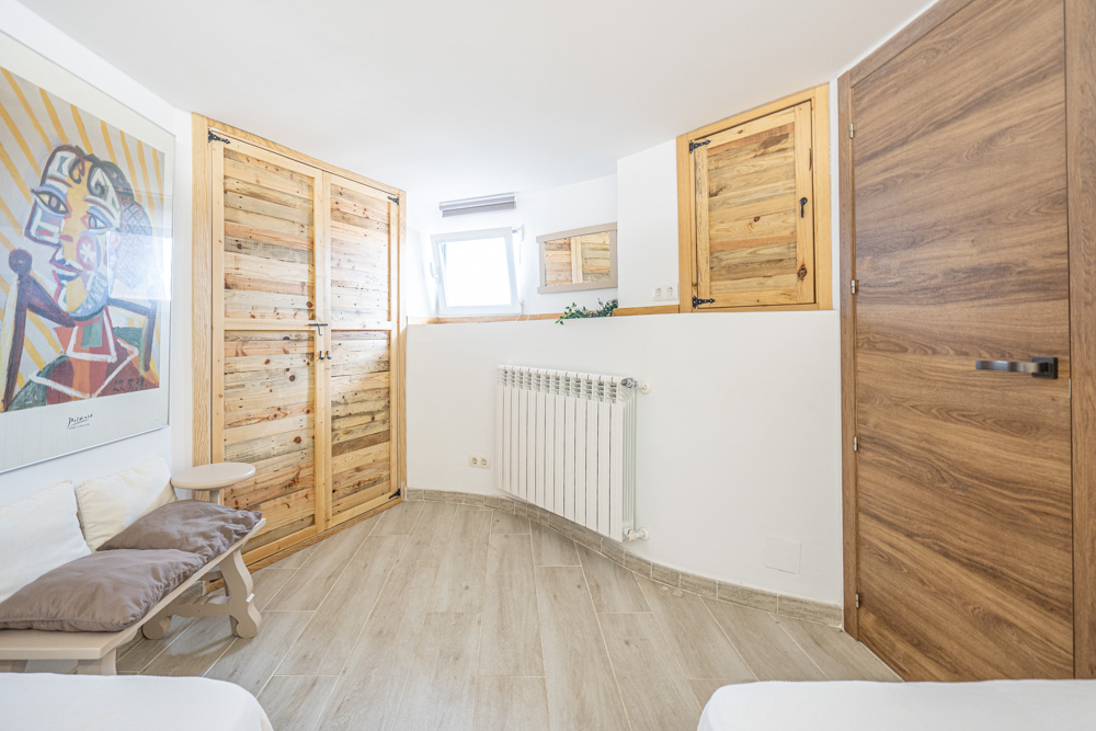 Bedroom featuring custom rustic wood closets, wood-effect tile flooring, a wall-mounted radiator, and natural light from a high-set window.