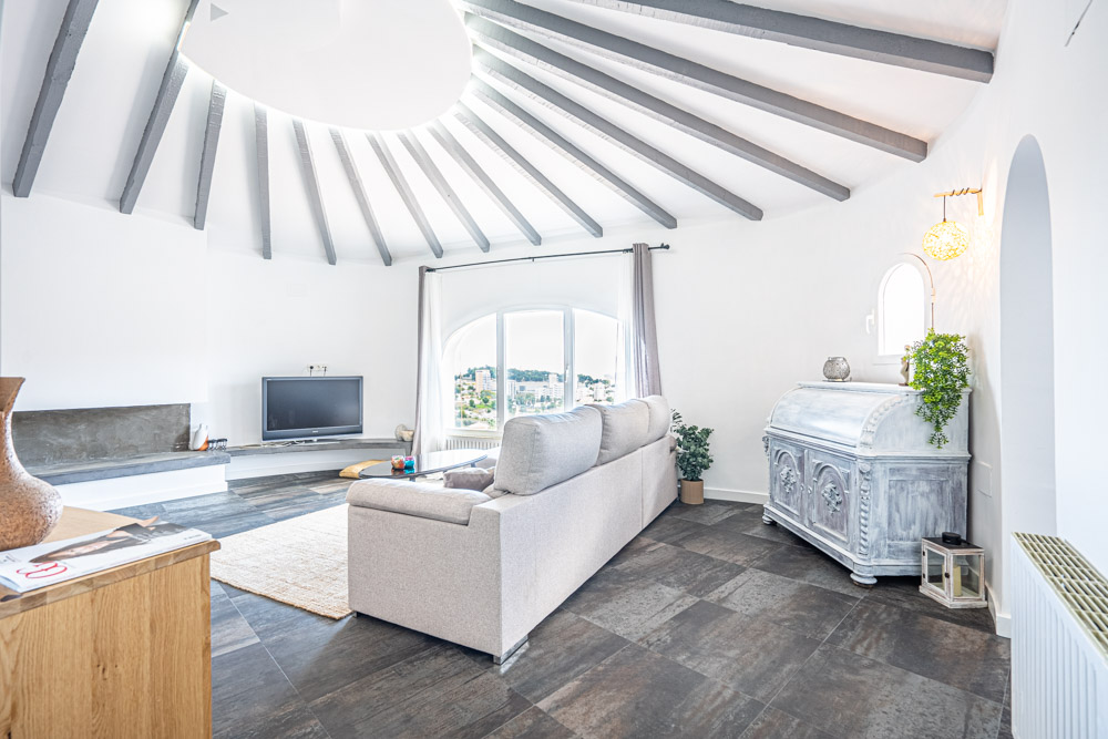 Circular living room featuring radiating exposed ceiling beams, a large arched window with town views, and dark stone-effect floor tiles.