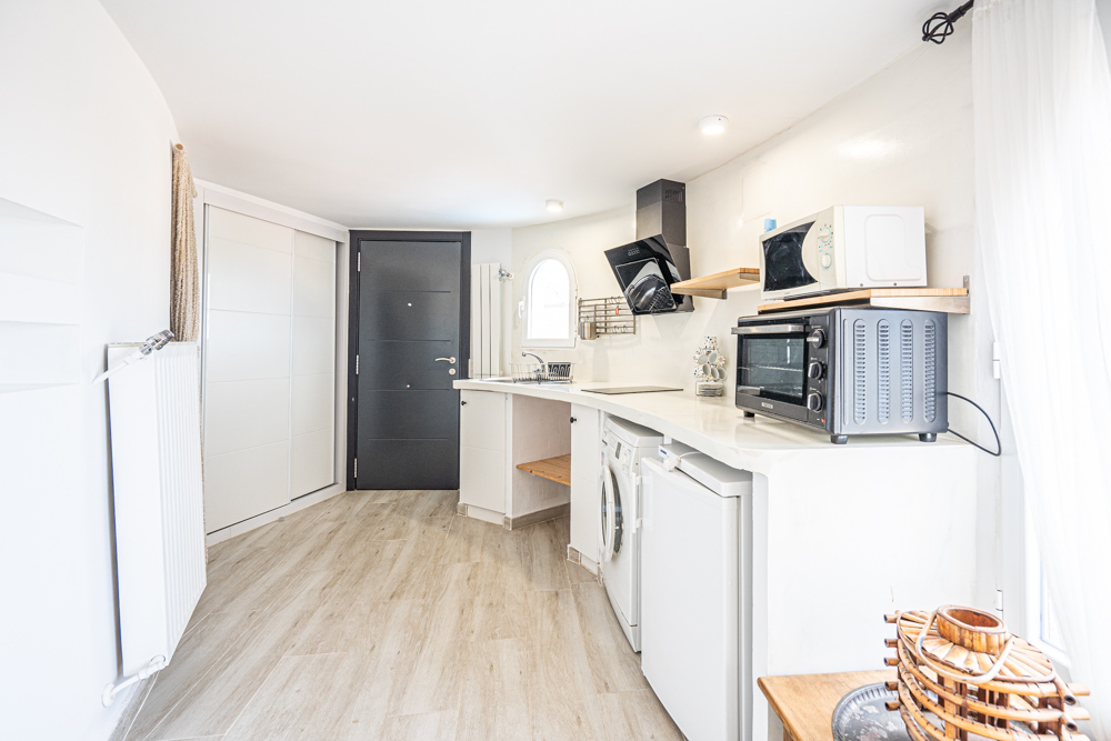 Compact renovated kitchen featuring a curved white countertop, modern appliances, wood-effect flooring, and a private entrance door.
