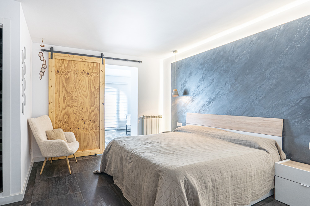 Modern bedroom featuring a blue textured accent wall with integrated LED lighting, dark tile flooring, and a rustic sliding wooden barn door.