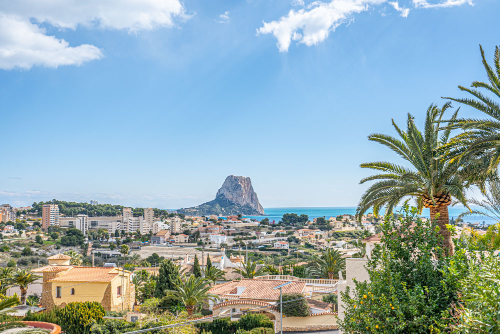 Panoramic view from the villa overlooking the Peñón de Ifach and the Mediterranean Sea, framed by palm trees and the coastal town of Calpe.