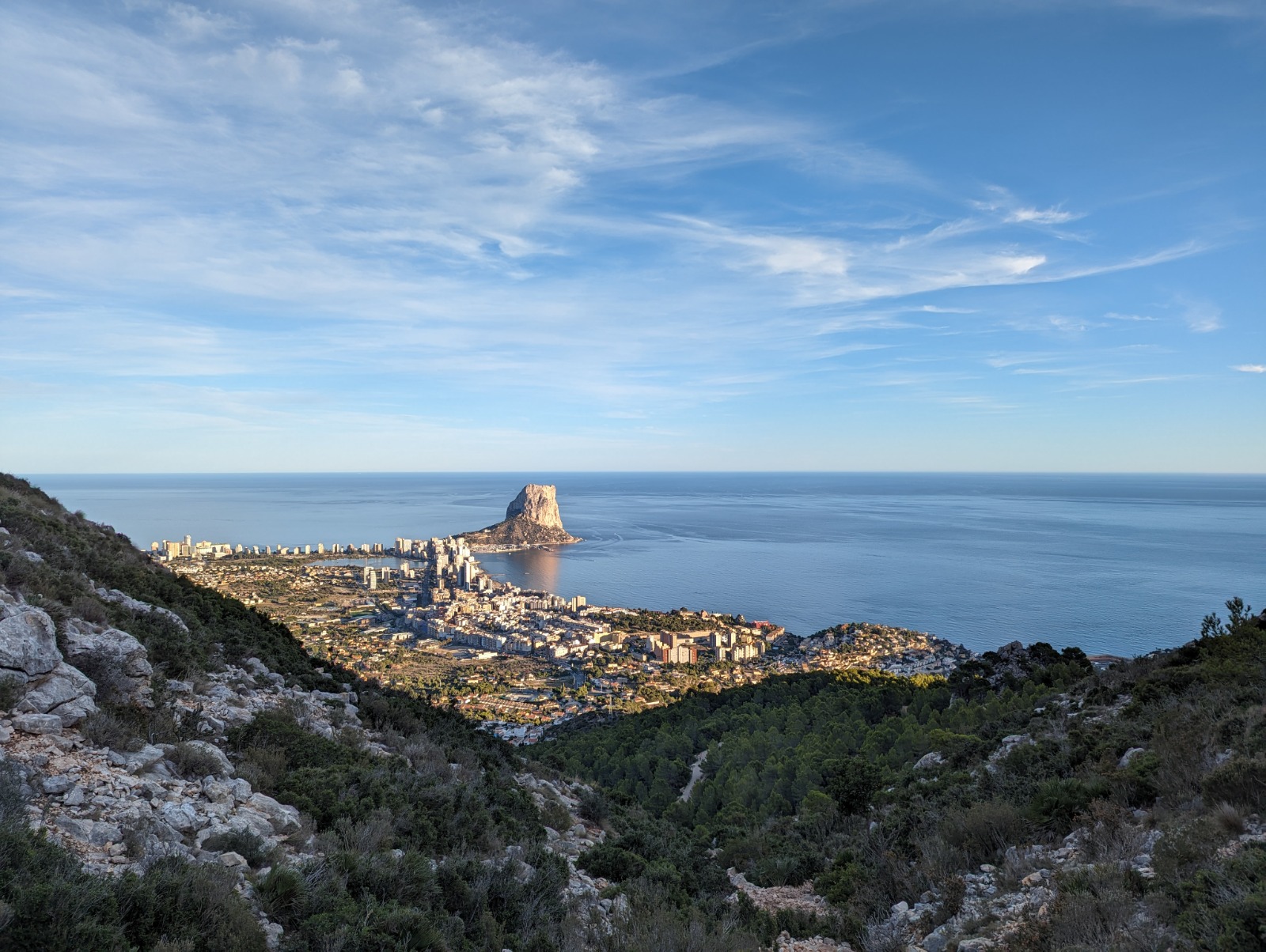 Panoramic view of the Peñón de Ifach and Calpe coastline from an elevated position, showcasing the Mediterranean Sea and rugged mountain terrain.