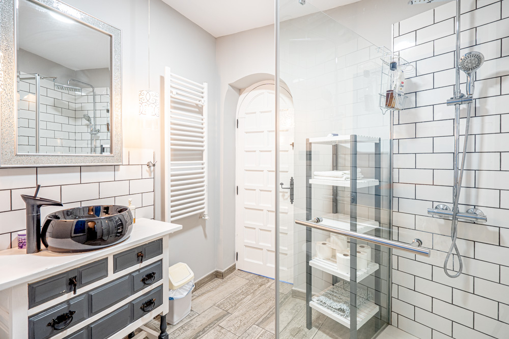 Renovated bathroom featuring a black vessel sink, rustic vanity, and a walk-in shower with white subway tiles and glass partition.